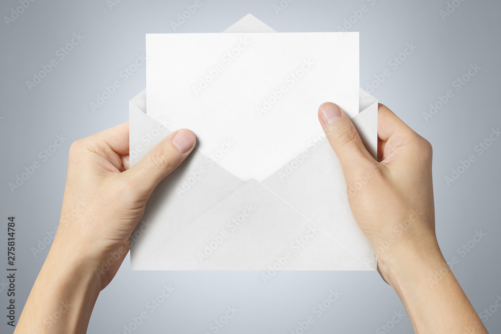 Hand holding an open white envelope with a blank paper inside on gray background Hand holding an open white envelope with a blank paper inside on gray background