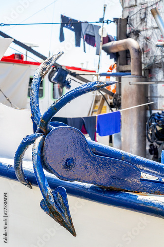 Close-up of an old dark blue anchor at a fishing boat in the Port of Kavala, Eastern Macedonia, Northern Greece, clothes hanging on clotheslines in the background