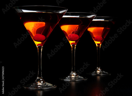 Group of three manhattan cocktails in bar on black