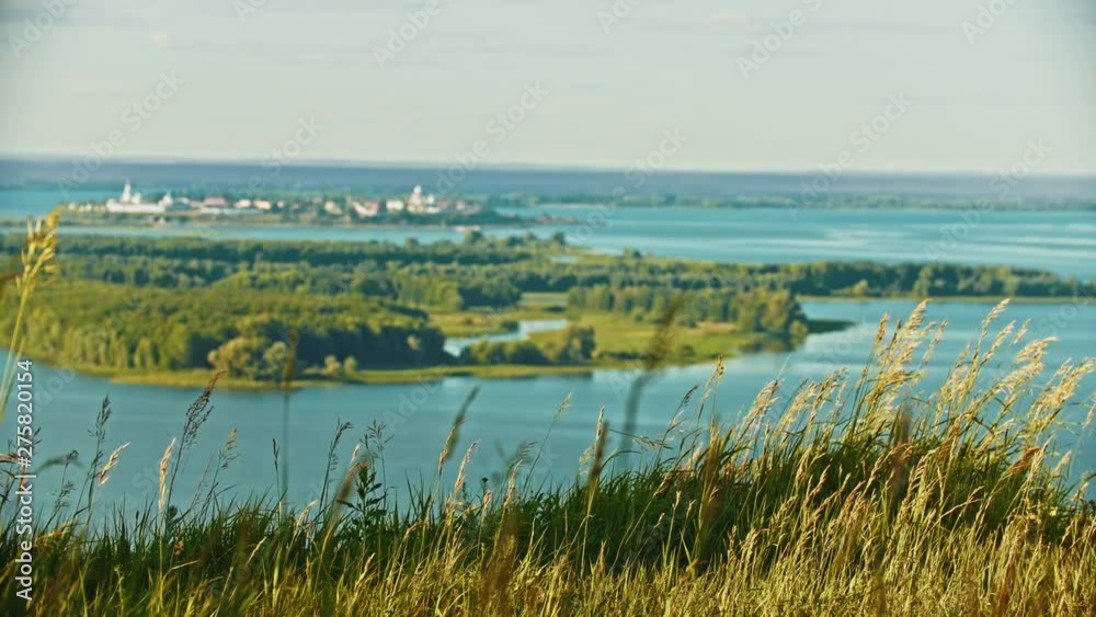 A landscape - grass and spikes fluttering in the wind - blurred view on a little town on the island A landscape - grass and spikes fluttering in the wind - blurred view on a little town on the island