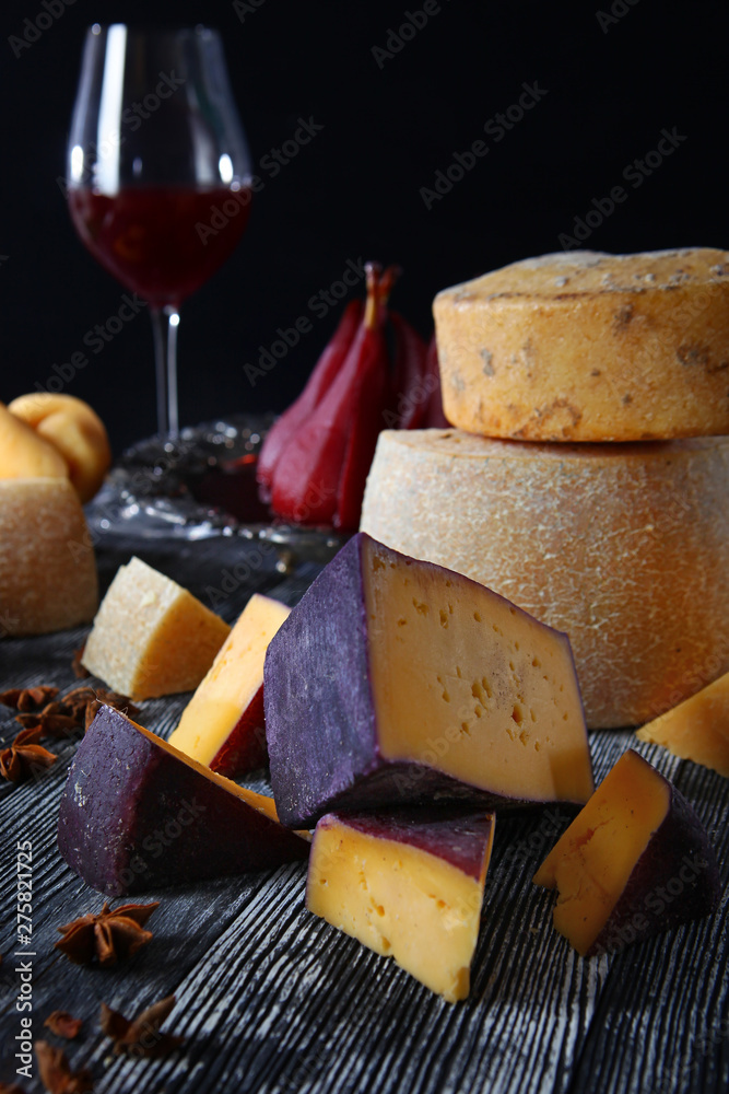 An assortment of hard craft cheeses on a wooden board and on a black background. Still life concept. Cheese production in small volumes.