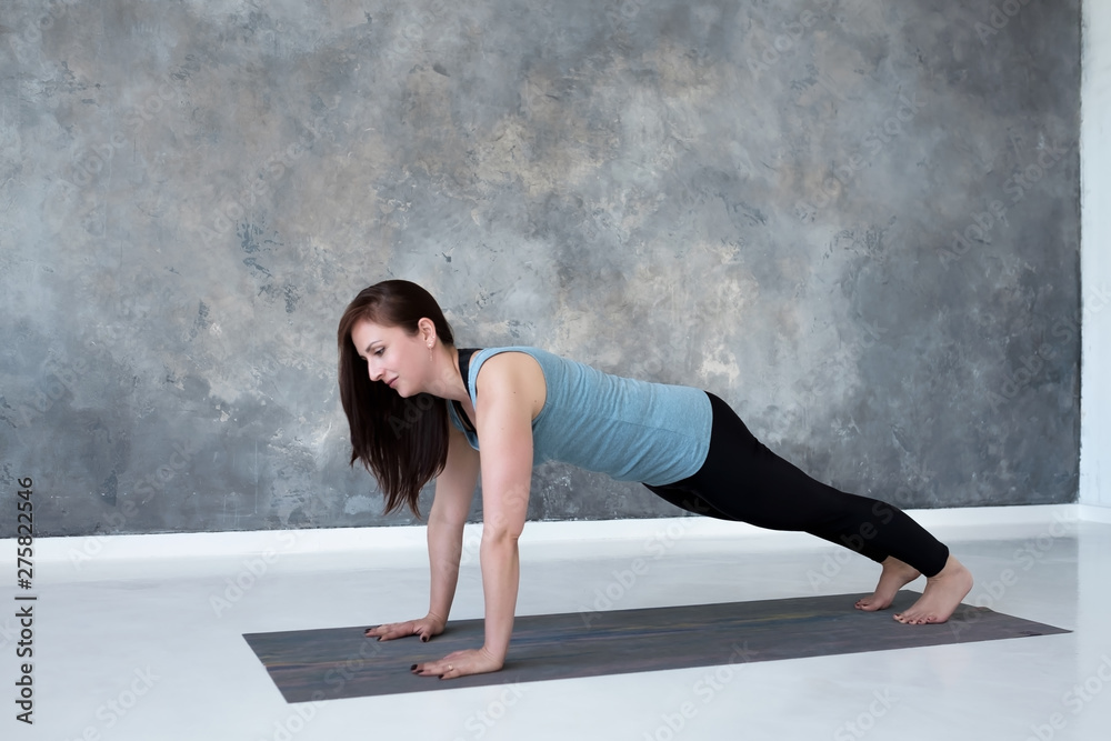 Young woman practicing yoga, doing Push ups or press ups exercise, phalankasana, Plank pose. Indoor full length