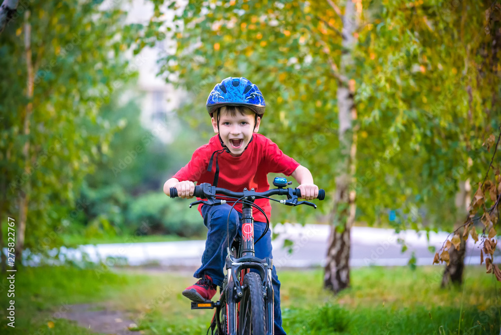 A small white Toddler boy in a protective helmet on his head sits on a children's bicycle. Toddler on a two-wheeled red bicycle looks forward. A sly smile on the child's face A small white Toddler boy in a protective helmet on his head sits on a children's bicycle. Toddler on a two-wheeled red bicycle looks forward. A sly smile on the child's face