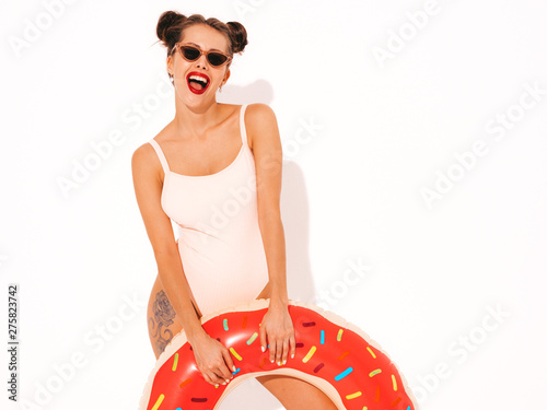 Young beautiful sexy smiling hipster woman with red lips in sunglasses.Girl in summer swimwear bathing suit with donut lilo inflatable mattress.Positive female going crazy.Funny model isolated