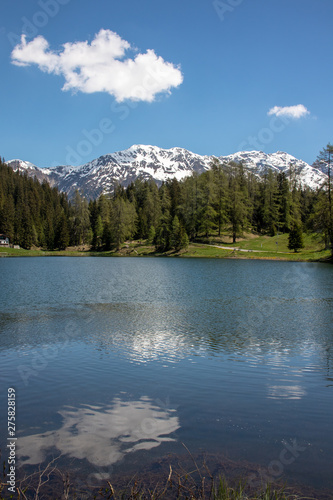 View of a small lake, green meadows in front of high mountains at blue sky in the Swiss Alps in the Davos / Kloster area.