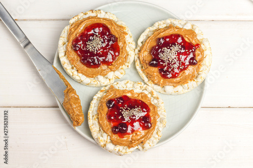 crunchy natural peanut butter strawberry jam jelly sandwich with chia seeds on rice cake bread. Proper nutrition diet vegetarian breakfast on plate next to knife with peanut butter