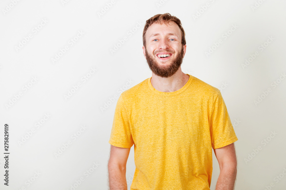 Portrait of young beard man in yellow shirt with blue eyes smiling laughing looking at camera over gray background. Portrait of young beard man in yellow shirt with blue eyes smiling laughing looking at camera over gray background.