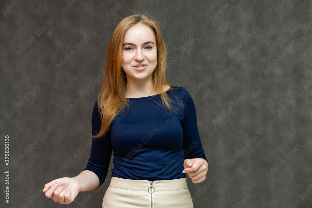 Portrait of a knee-high beautiful pretty red-haired woman girl in a blue jacket with a light skirt on a gray background in the studio. Smiles, shows emotions, talks, spreads his hands. Portrait of a knee-high beautiful pretty red-haired woman girl in a blue jacket with a light skirt on a gray background in the studio. Smiles, shows emotions, talks, spreads his hands.