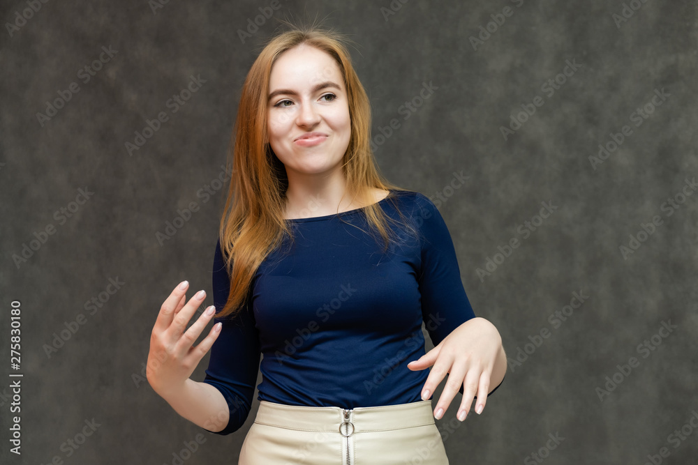 Portrait of a knee-high beautiful pretty red-haired woman girl in a blue jacket with a light skirt on a gray background in the studio. Smiles, shows emotions, talks, spreads his hands. Portrait of a knee-high beautiful pretty red-haired woman girl in a blue jacket with a light skirt on a gray background in the studio. Smiles, shows emotions, talks, spreads his hands.