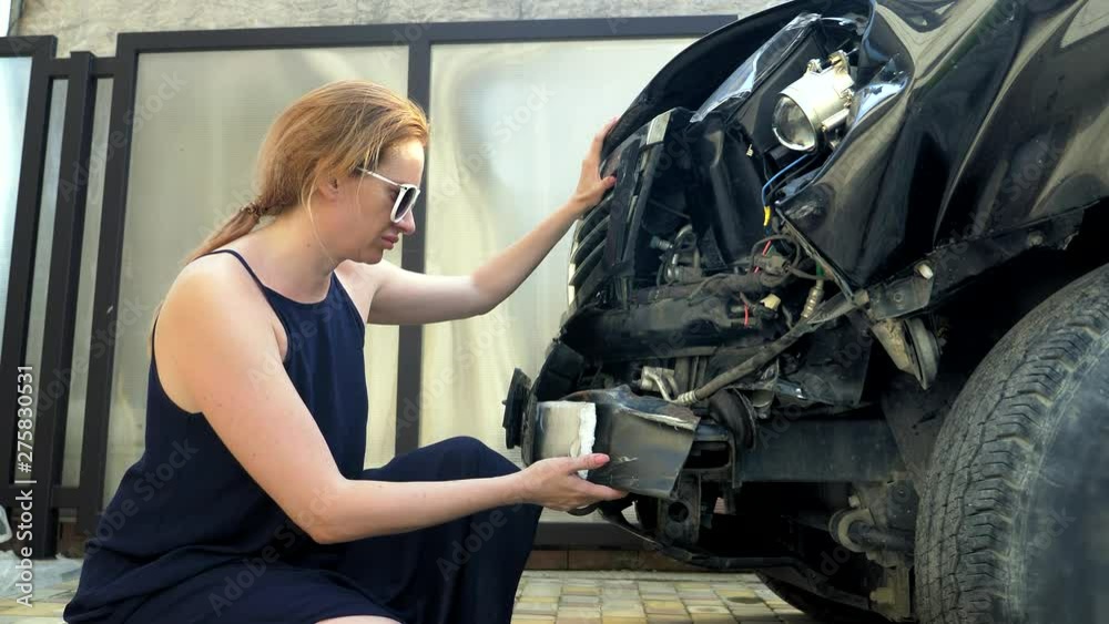 Displeased woman sitting near a car with a broken bumper. car accident concept Displeased woman sitting near a car with a broken bumper. car accident concept