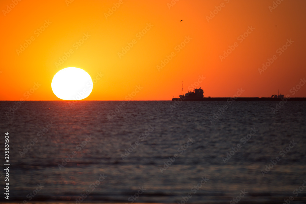 the sun disk sets against the background of the ships standing in the raid