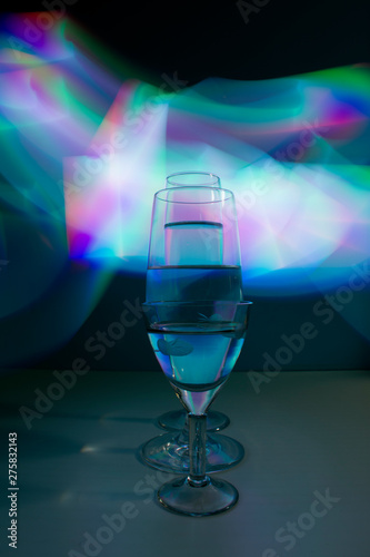 A three wine glass isolated on a black background with red, white, pink and orange neon light painting streaks of light behind them. Light wave, play of color, drawing with light.