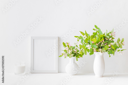 Mockup with a white frame and branches with green leaves in a vase on a white table