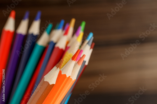 Pens and pencils in metal holder in front of wall background