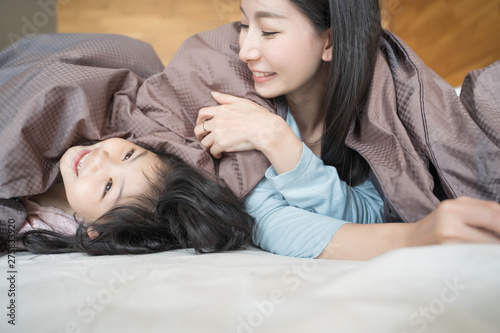 Mother and her daughter child girl playing in the bedroom and putting blanket on . Happy Asian family