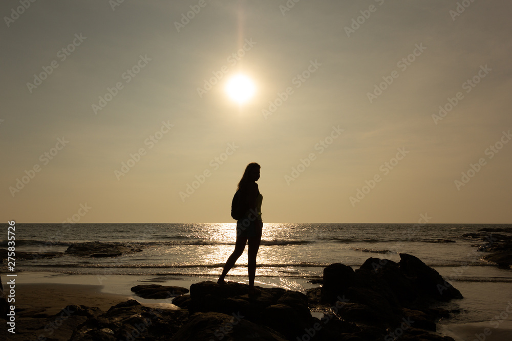 Silhouette of a young woman against the background of the sea and the sun