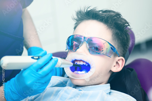 A boy with goggles in the dental chair. Mouth directed lightpolymerization lamp with blue light for sustainable fillings.