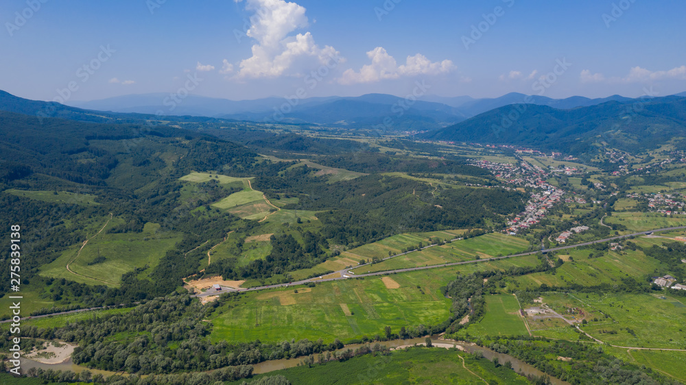 Aerial view of the Carpathian mountains. Natural background with geometric pattern - beige and red rectangles of the fields and roofs and lines of roads and trees. Zakarpattia, Ukraine.