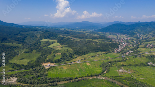 Aerial view of the Carpathian mountains. Natural background with geometric pattern - beige and red rectangles of the fields and roofs and lines of roads and trees. Zakarpattia, Ukraine.