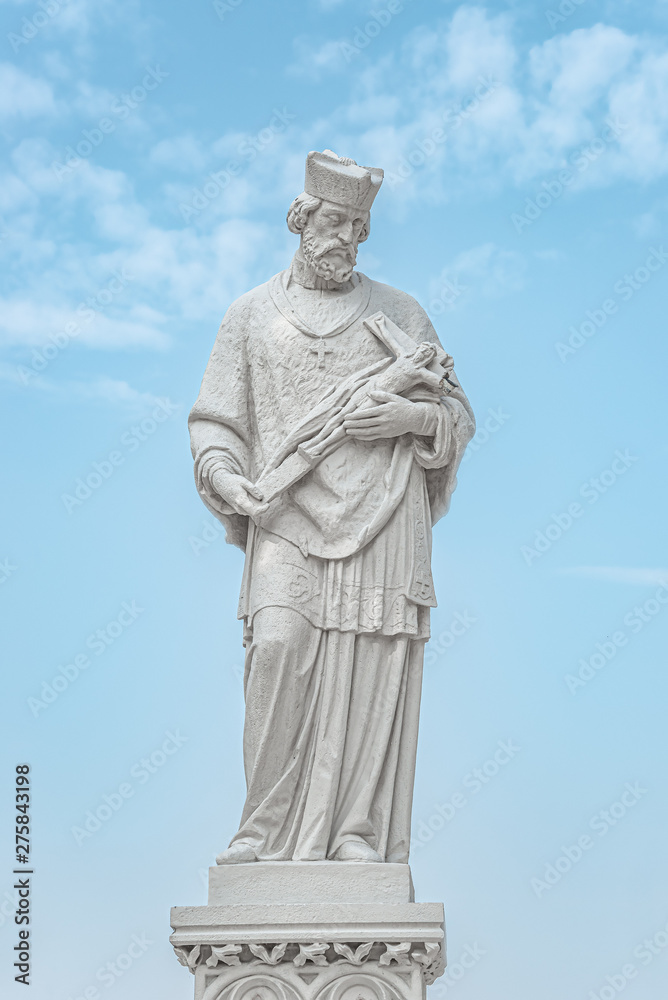 Statue of priest with figure of crucified Jesus in Vienna downtown at blue sky background, Austria
