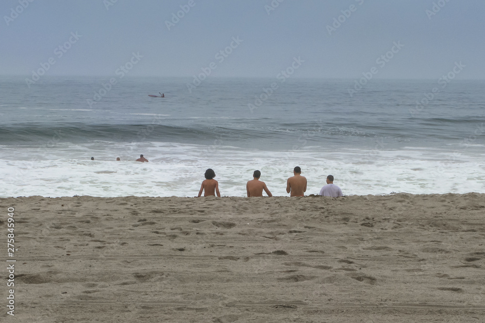 Group of friends sitting on the sandy beach, enjoying the view of the ocean. Beach holidays. Calm and tranquility.