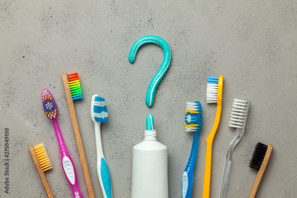Toothpaste in the form of a question mark and many different and colored toothbrushes. Concept