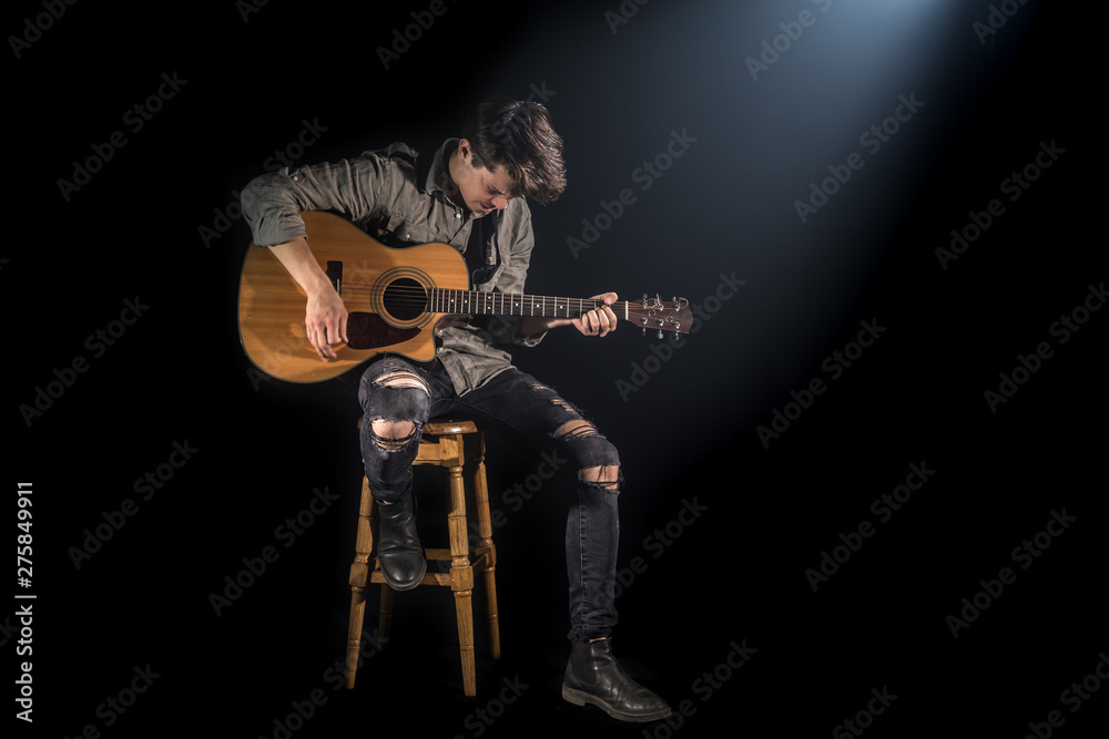 musician playing acoustic guitar, sitting on high chair, black background with beautiful soft light