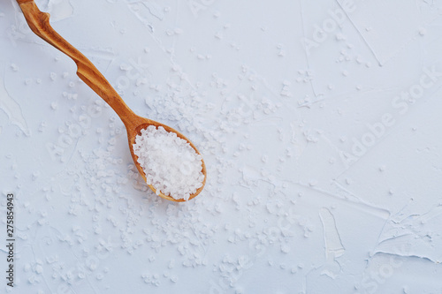 Iodised coarse sea salt in wooden spoon on blue background. Top view. Close up.