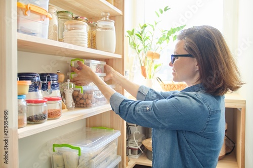 Interior of wooden pantry with products for cooking. Adult woman taking kitchenware and food from the shelves photo