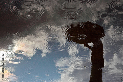 reflection of a man with an umbrella in a puddle