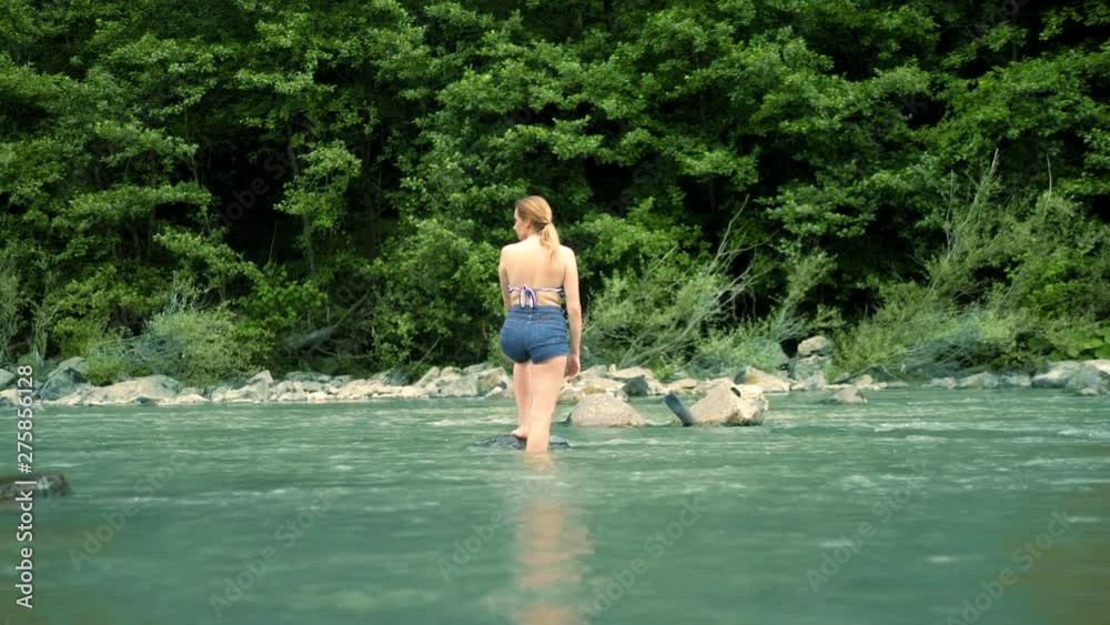 summer holiday concept. a woman in a bathing suit and shorts goes over a mountain river to a ford summer holiday concept. a woman in a bathing suit and shorts goes over a mountain river to a ford