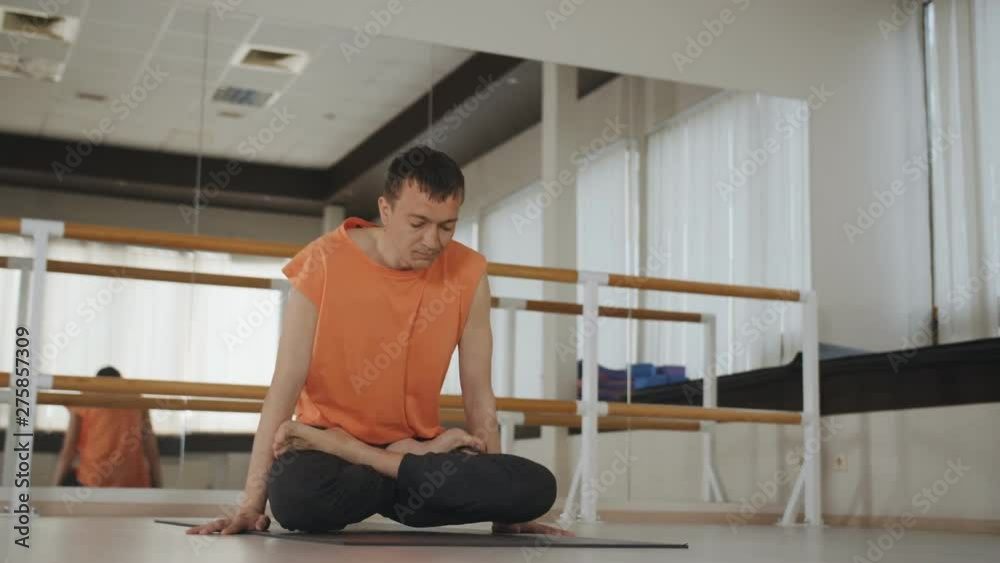 Young sporty man doing ashtanga yoga in studio. Guy doing an asana on black mat indoors near a mirror, lifestyle healthy concept.