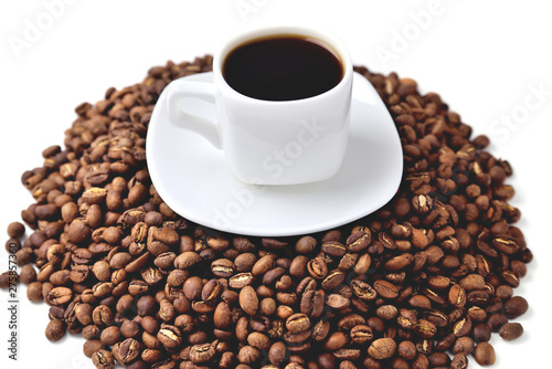 white cup of coffee on a white saucer stands on a hill of coffee beans on a white background angle view from above