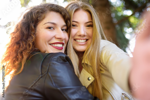 Two beautiful young women take selfie on sunny park. Girlfriends.