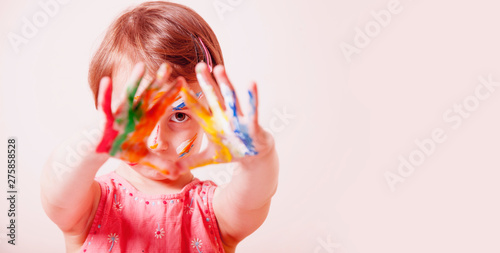 Little cute girl with children's colorful makeup showing painted hands. Happy childhood and art concept. Selective focus on eyes.