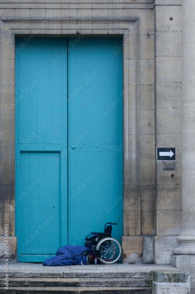 Homeless handicapped person sleeps in a blue doorway in Europe. 