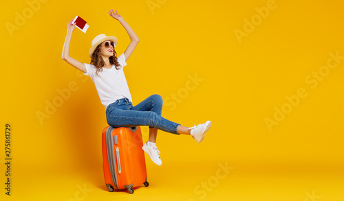 concept of travel. happy woman girl with suitcase and  passport on  yellow background.