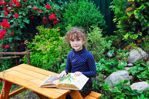 landscaping green garden with flowers and an Alpine slide, in the foreground girl sitting at a wooden table on a bench and reading a book on gardening.