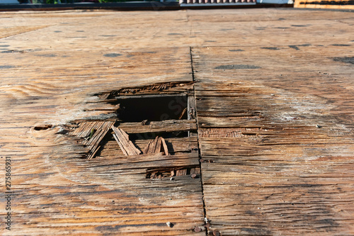 Plywood decking damage and water stains from rain water standing, leaking on roof sheathing near downspout hole. Flat roof inspection, repair and replacement project in progress