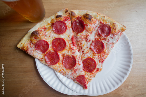two slices of pepperoni pizza on a plate with a beer