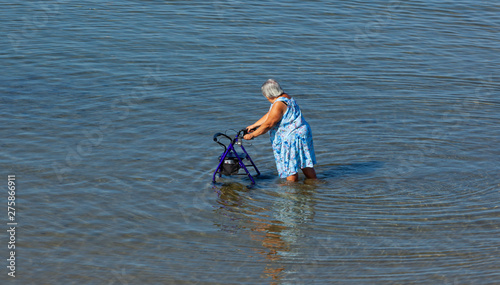 Elderly lady walks with walker in the sea.