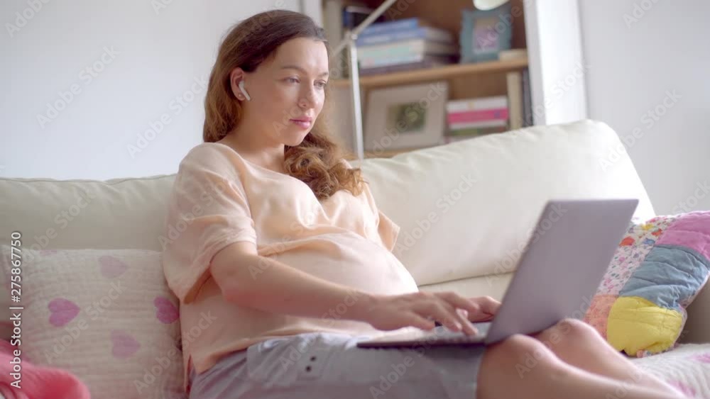Portrait of a young beautiful pregnant woman sitting on a sofa with a laptop computer in her hands. Pregnant businesswoman working online at home. Portrait of a young beautiful pregnant woman sitting on a sofa with a laptop computer in her hands. Pregnant businesswoman working online at home.