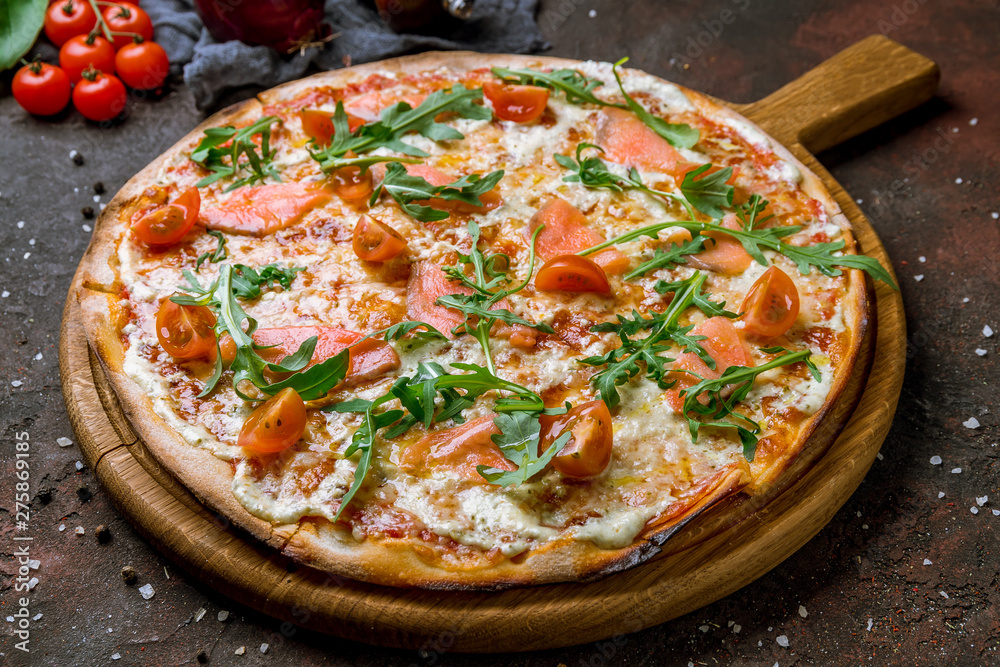 Pizza with salmon, tomatoes and aragula on dark concrete rustic background