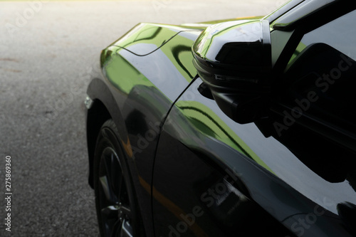 The side of a luxurious black car with a mirror that folds in the car park.