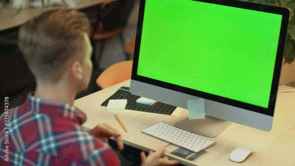 Young man call video online on computer with green screen in office Young man call video online on computer with green screen in office