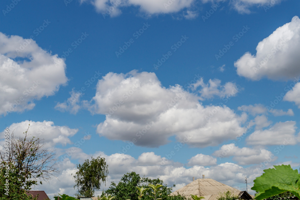 Blue sky and beautiful cloud with roofs of houses of the village. Plain landscape background for summer poster. The vast blue sky, bright colors, partial clouds