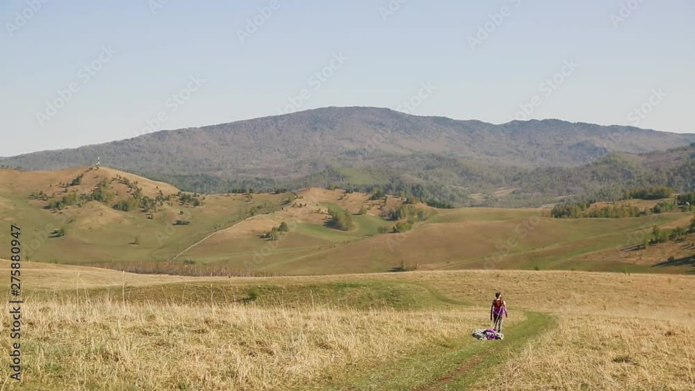 man with beard mustache striped white-yellow T-shirt and a green hat jeans with a red backpack. Carries a purple gray parachute on background of the mountains, a tattoo on his arm man with beard mustache striped white-yellow T-shirt and a green hat jeans with a red backpack. Carries a purple gray parachute on background of the mountains, a tattoo on his arm