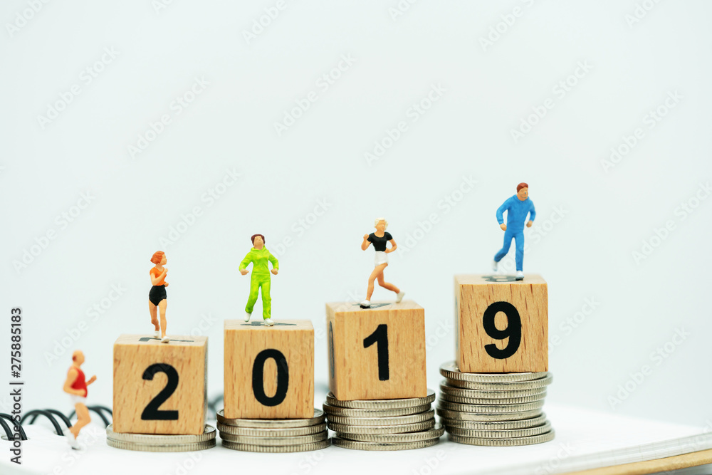 Miniature people running on a wooden box with number 2019 and coins. Miniature people running on a wooden box with number 2019 and coins.