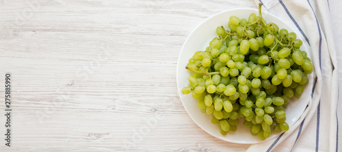 Green grape on a white plate over white wooden surface, top view. Space for text.