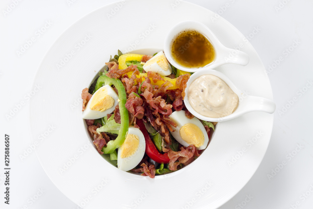 Fresh Caesar Salad with Deep-fried Bacon and Boiled Eggs & Mayonnaise on White Porcelain Circle Dish, Isolated on White Background with Shadow. Close-up Top View, Selective Focus at Food.